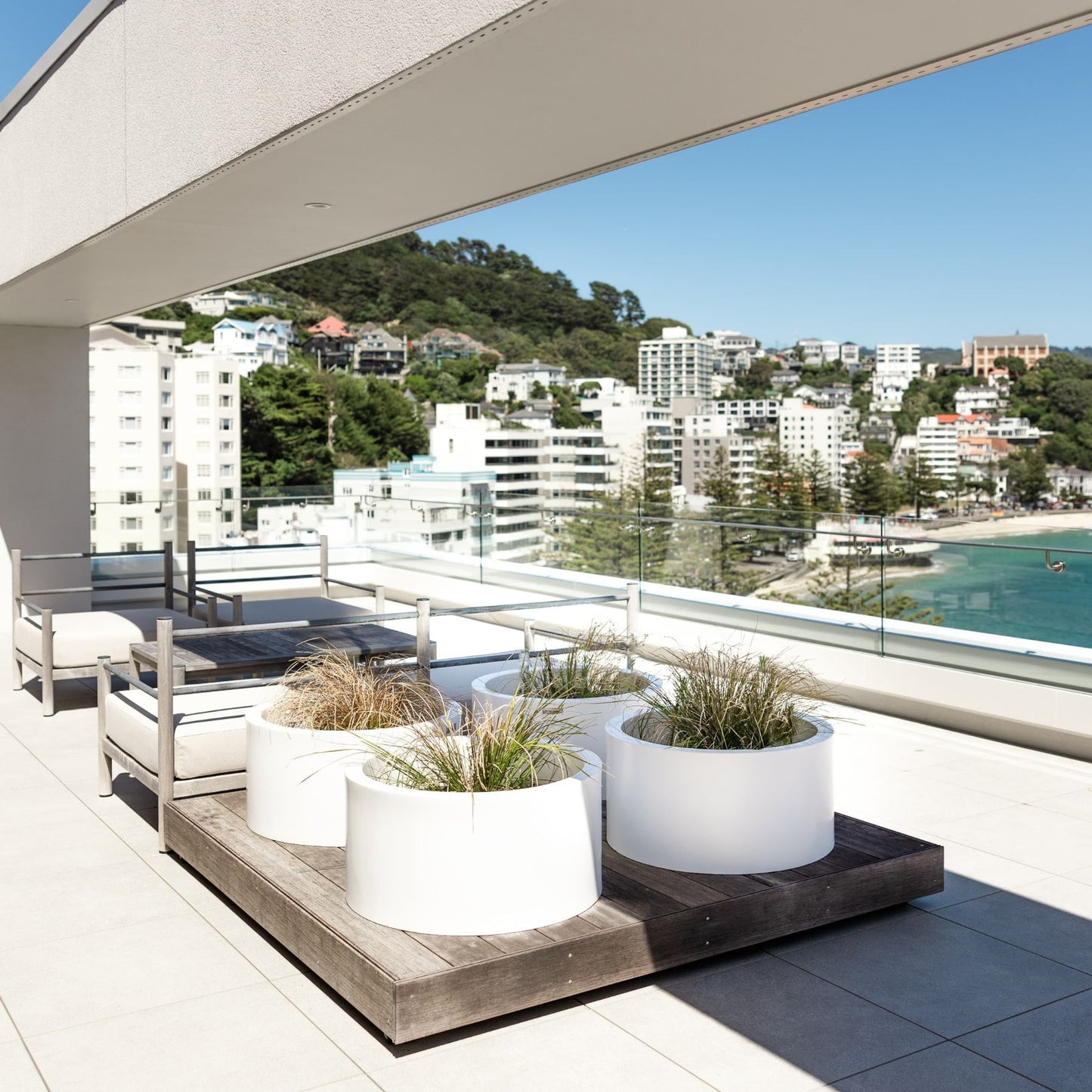 White cylinder planter pots on a balcony overlooking a bay.