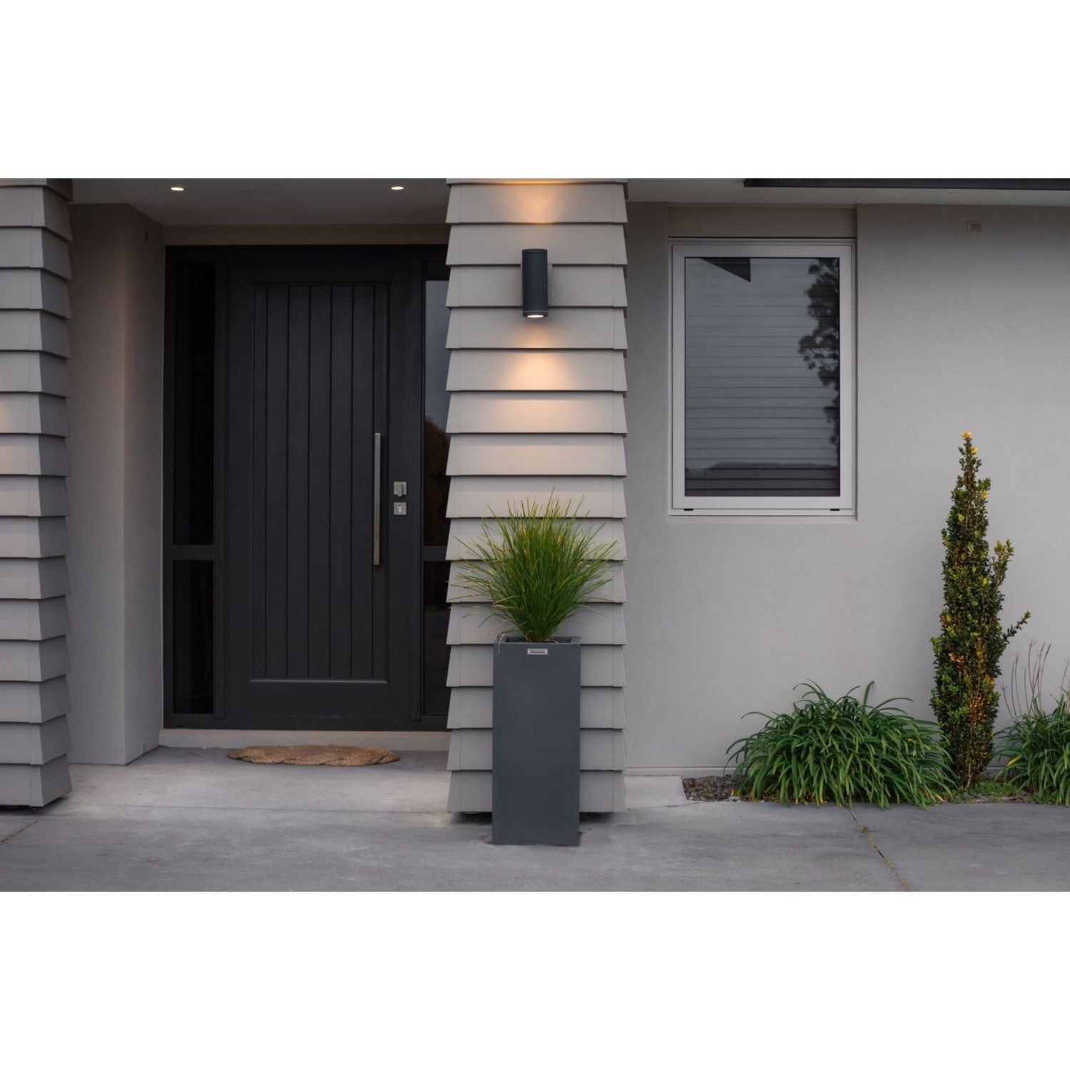 Dark grey square pot planter by a house entrance pillar.