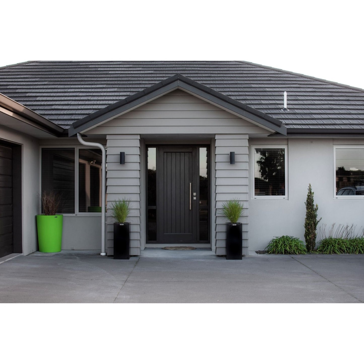 Lime green and black planter pots at a house entrance planted with grasses.