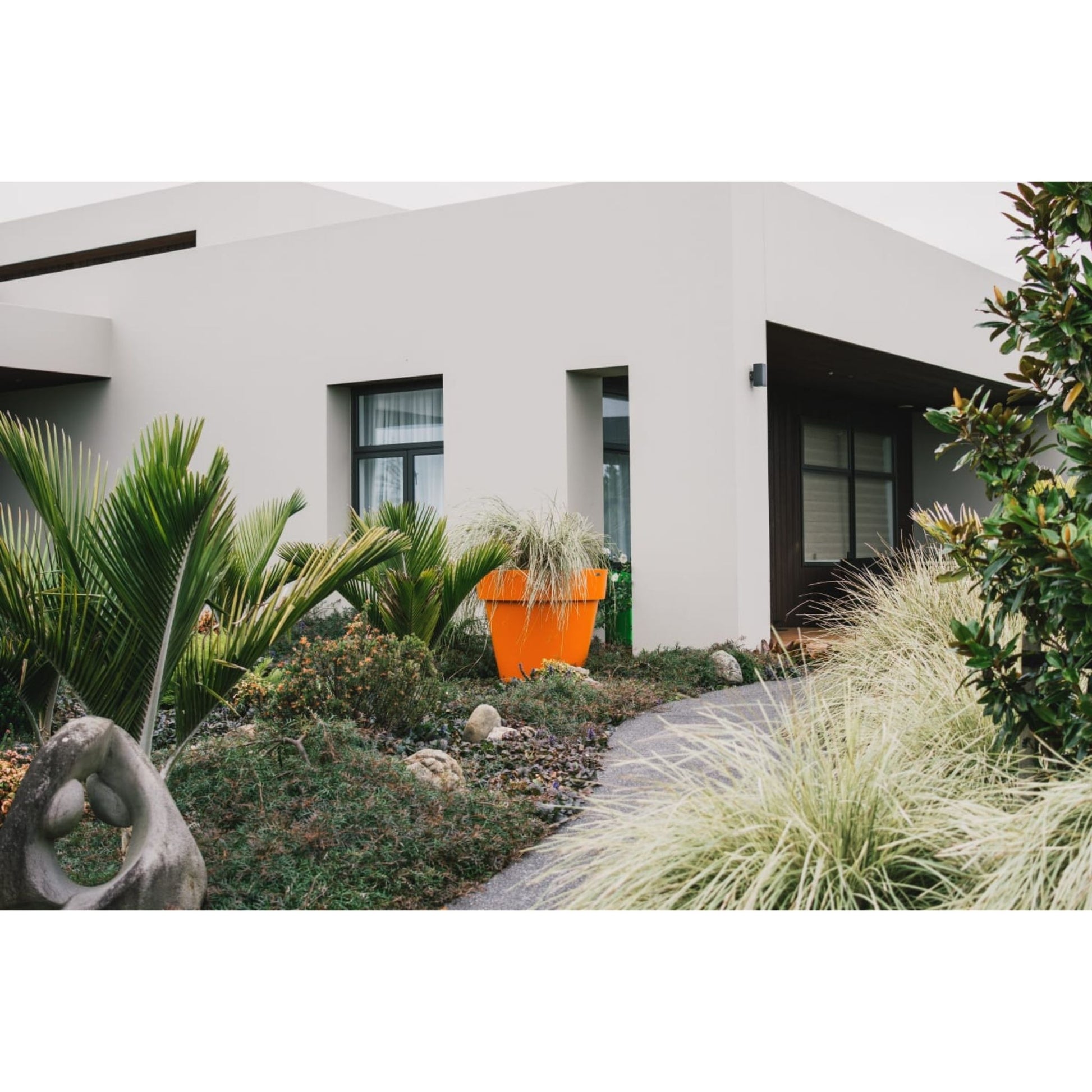 Large orange feature planter pot in a garden in front of a large house.