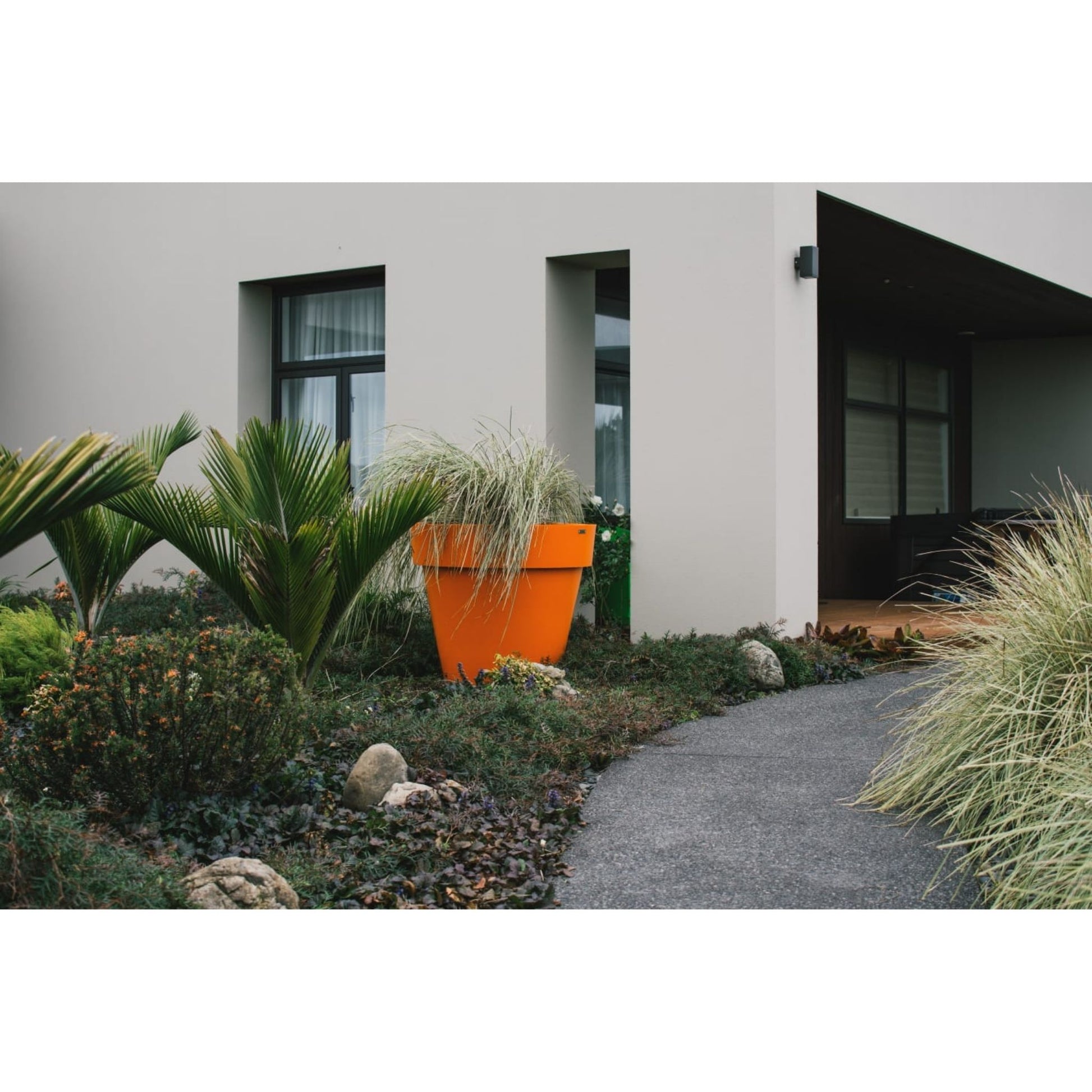 Large orange feature planter pot in a garden in front of a large house.