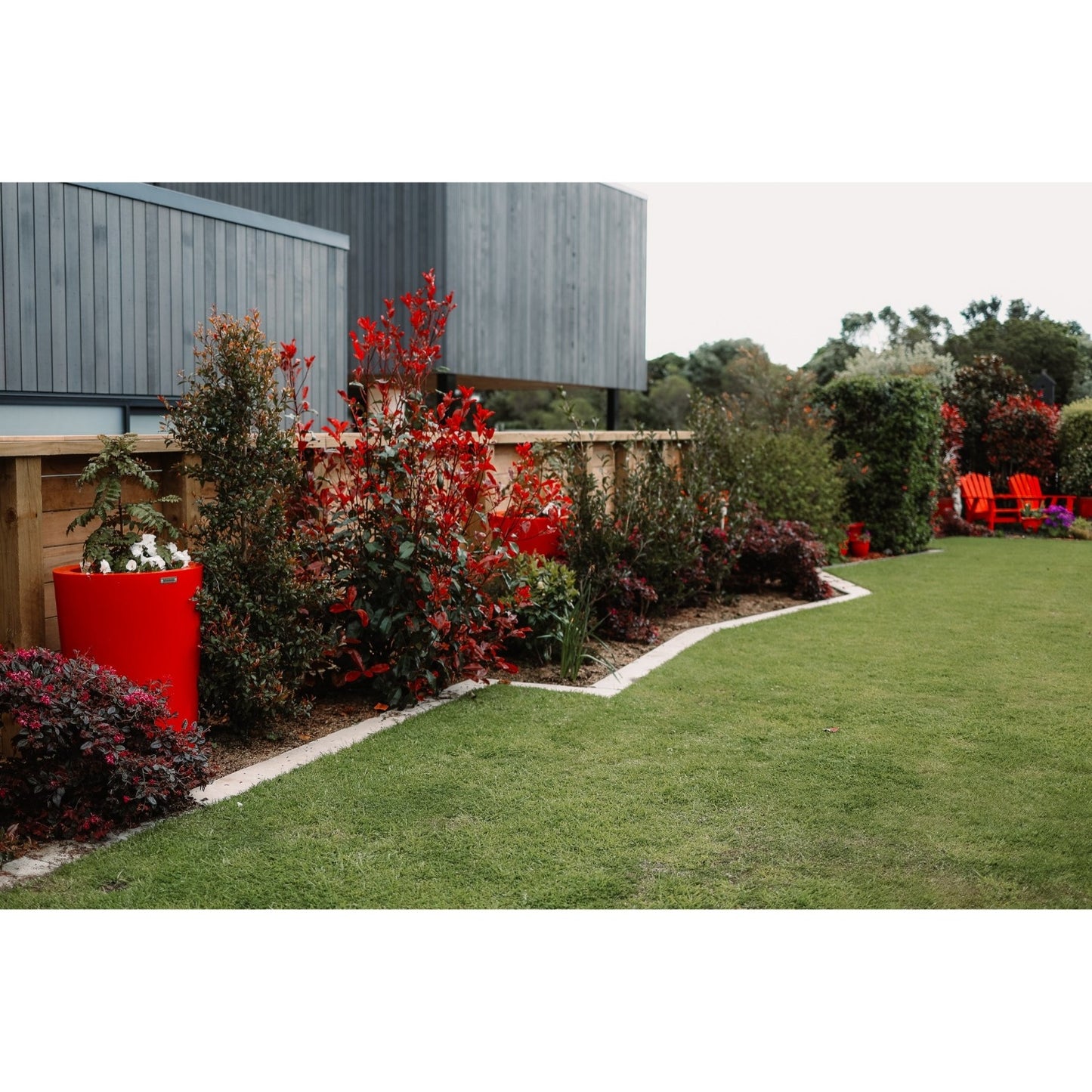 A stunning red planter pot sits in a garden amongst the plants.