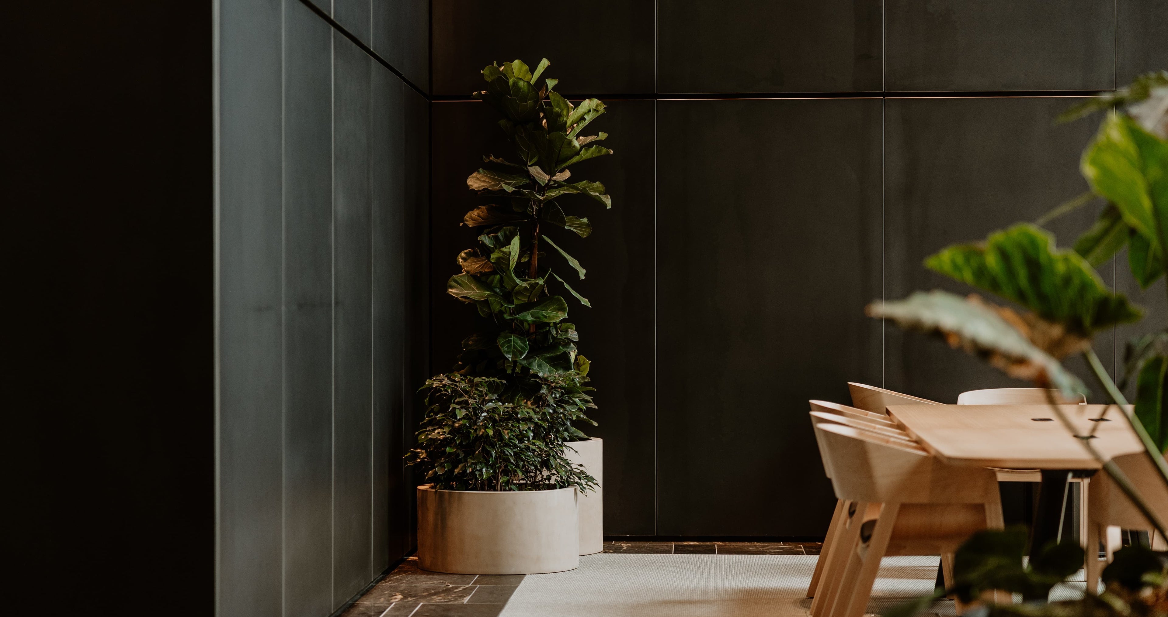 Modern interior with a wooden dining table and chairs against a dark tiled wall.