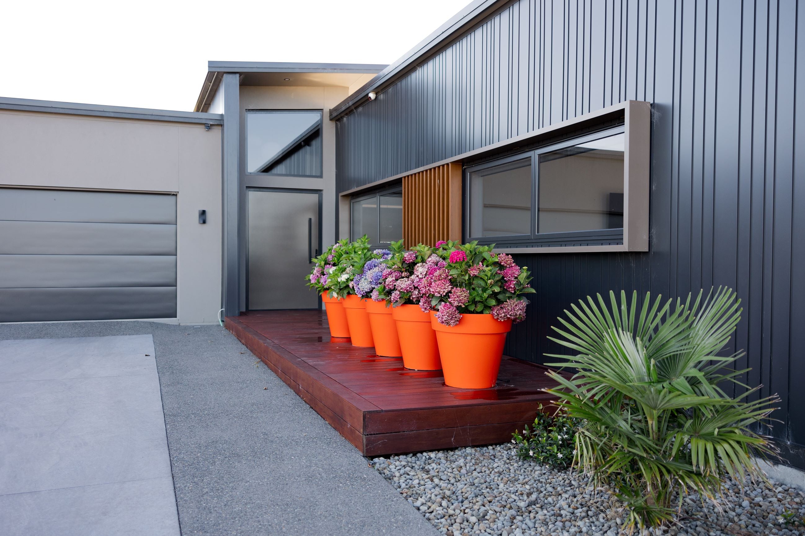 A row of orange Modscene planters sitting on a wooden deck in front of a house.