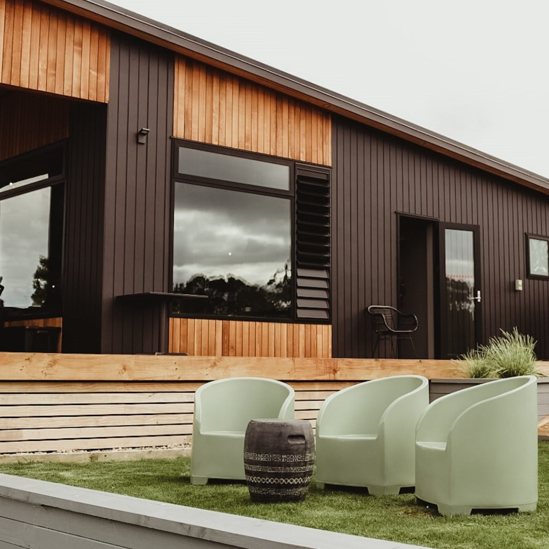 Modern house exterior with green outdoor chairs and a small table.