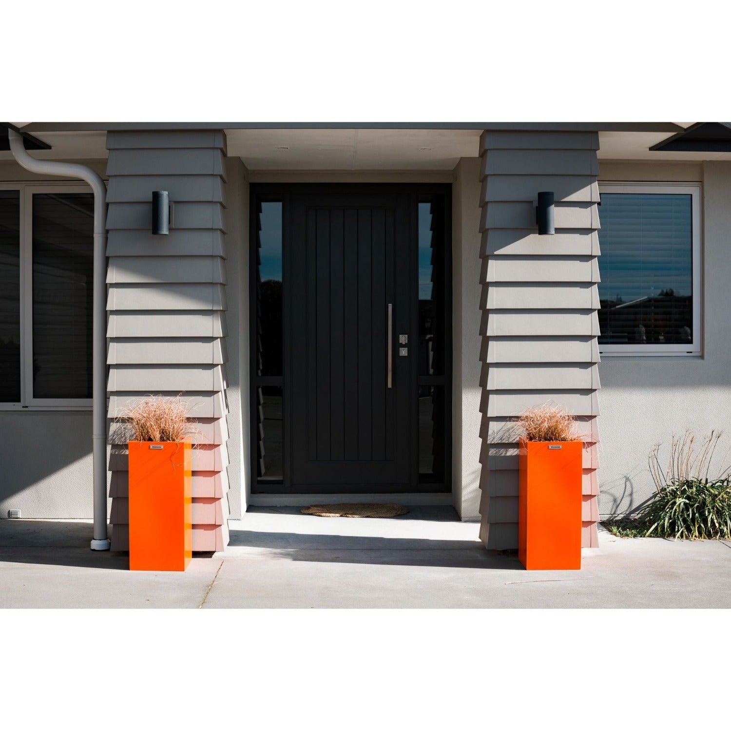 Two orange pot planters in front of house pillars.