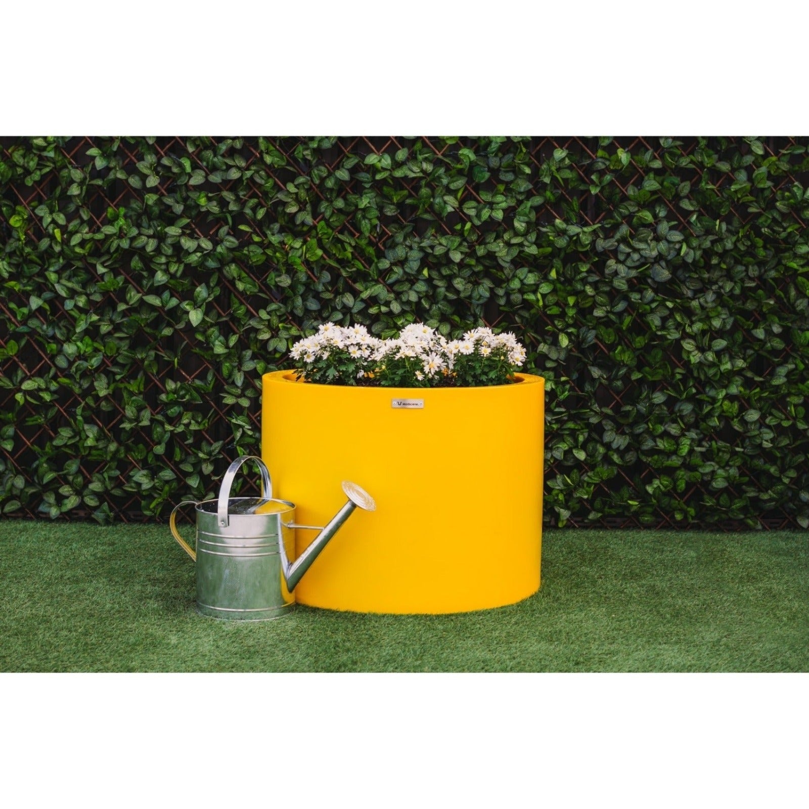 Large yellow planter pot pictured by a watering can on a lawn.