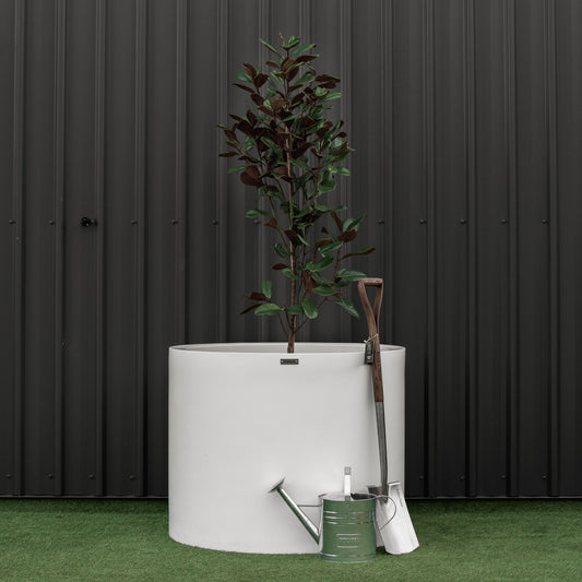 Giant white cylinder planter pot with a spade and watering can.