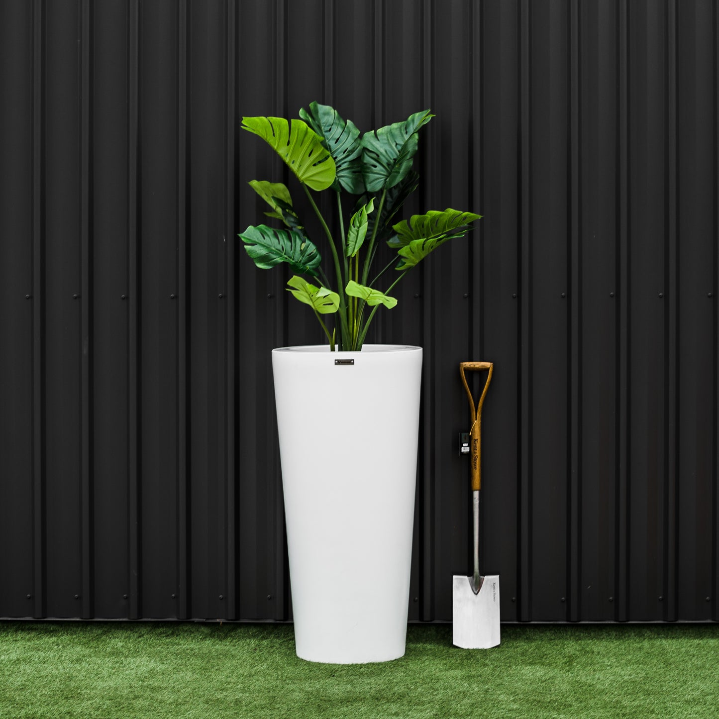 A large white Modscene planter pot on a lawn in front of a building wall. The planter is a large white modern planter and is New Zealand made.
