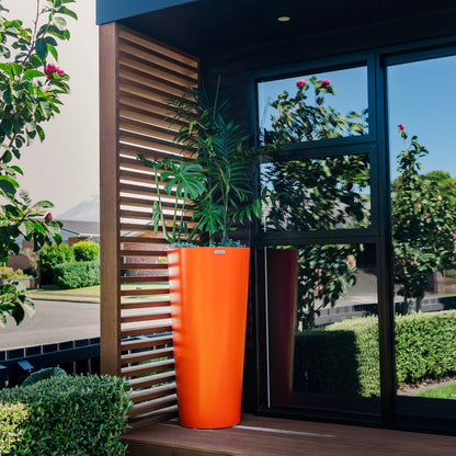 A large orange Modscene planter sits on an office balcony. The planter is planted with multiple plants which makes for a stunning pot creation.