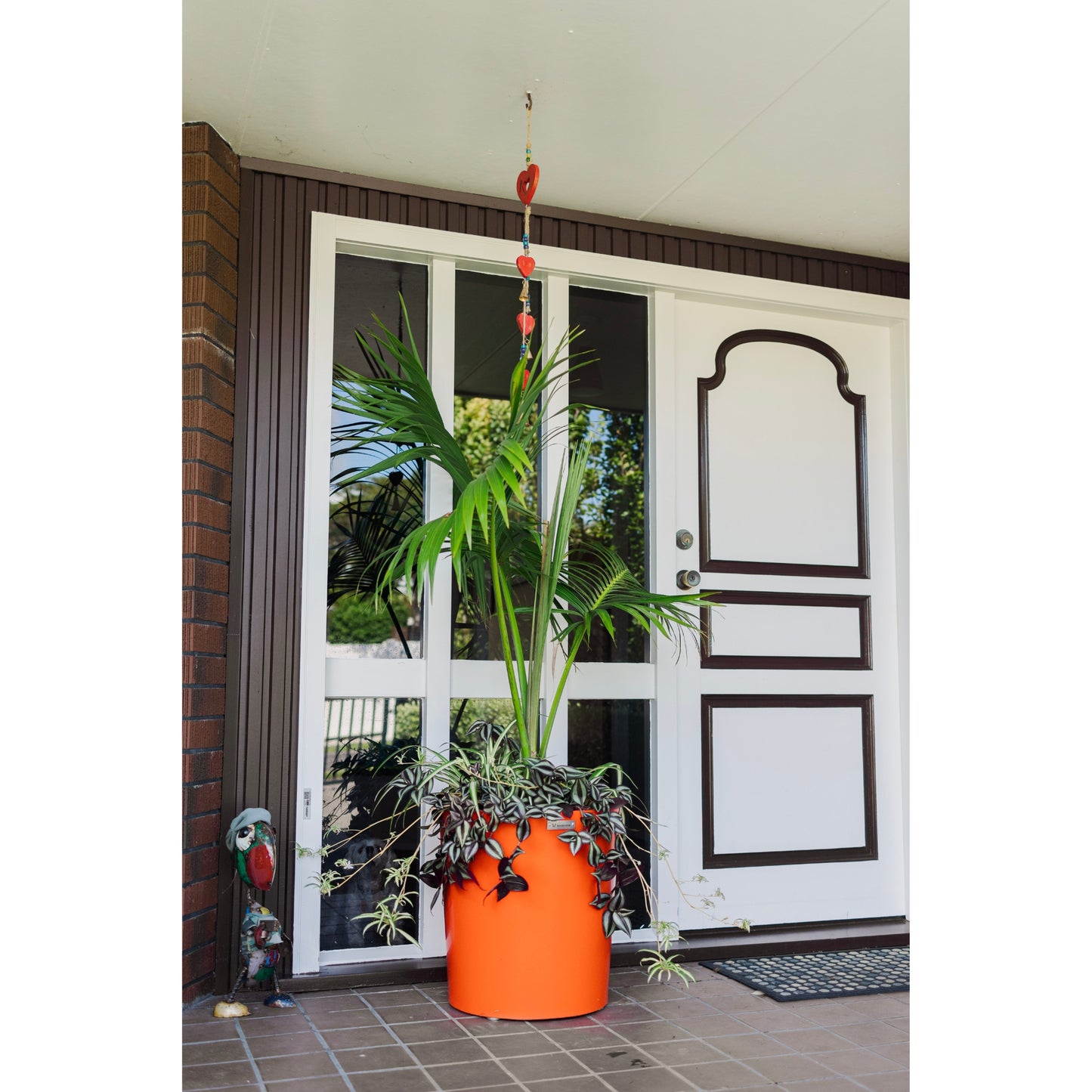 Orange Modscene planter pot by a front door. The planter is bright orange and has a palm in it.