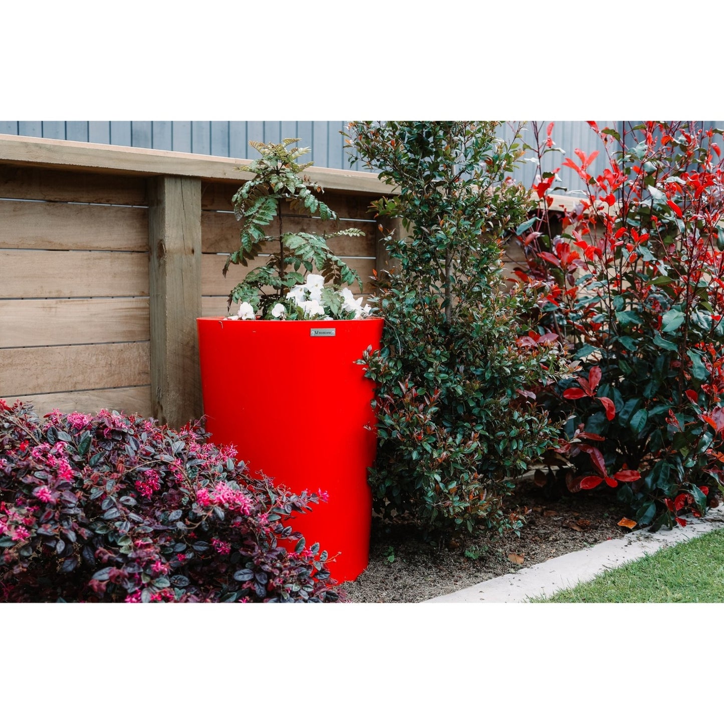 A stunning red planter pot sits in a garden amongst the plants.