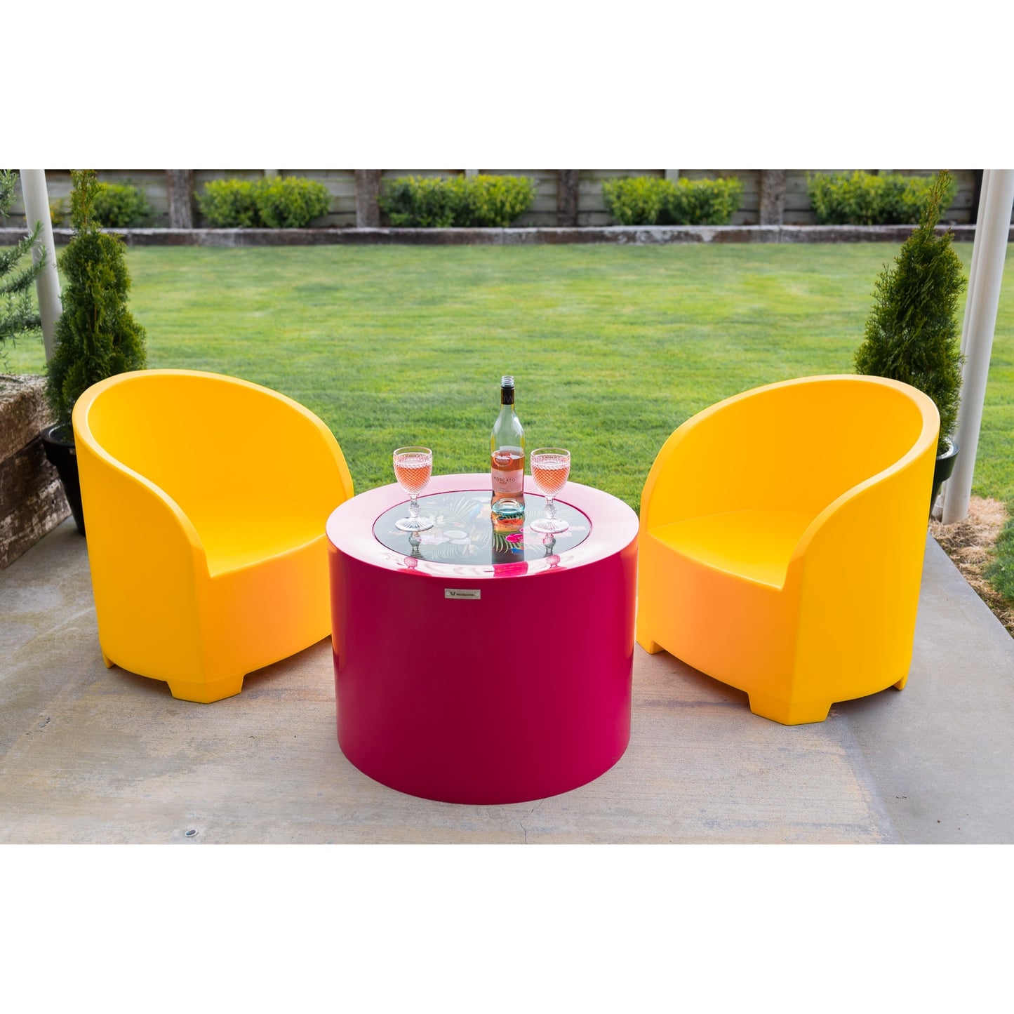Two yellow chairs and a pink outdoor table on a concrete patio area.